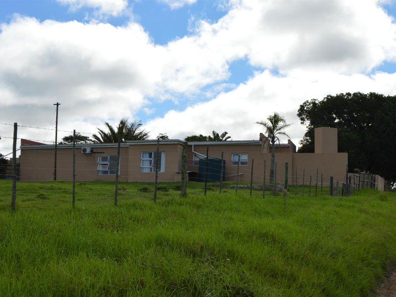 Rear view of the property showing the exterior facade, perimeter fencing, and water storage infrastructure set against a grassy landscape.