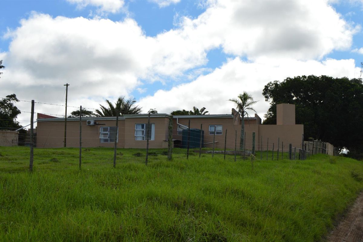 Rear view of the property showing the exterior facade, perimeter fencing, and water storage infrastructure set against a grassy landscape.
