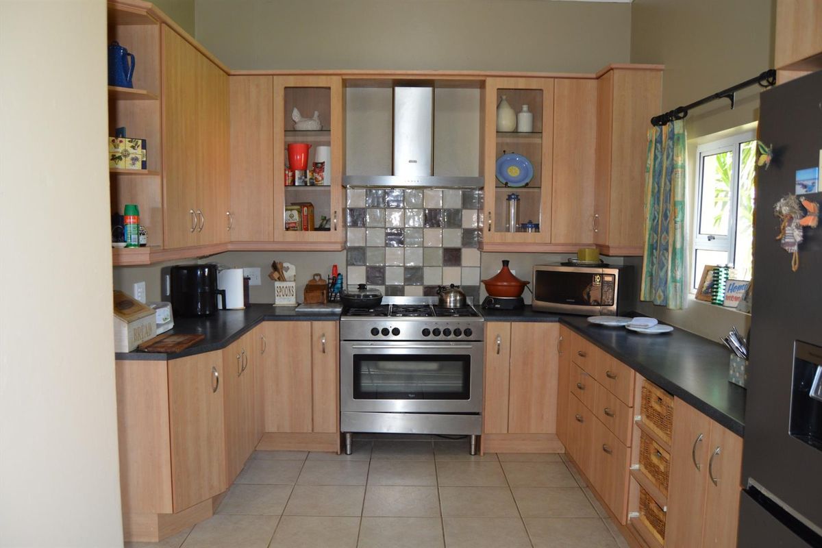A functional kitchen featuring light wood cabinetry, stainless steel gas stove, extractor fan, tiled backsplash, and dark laminate countertops.