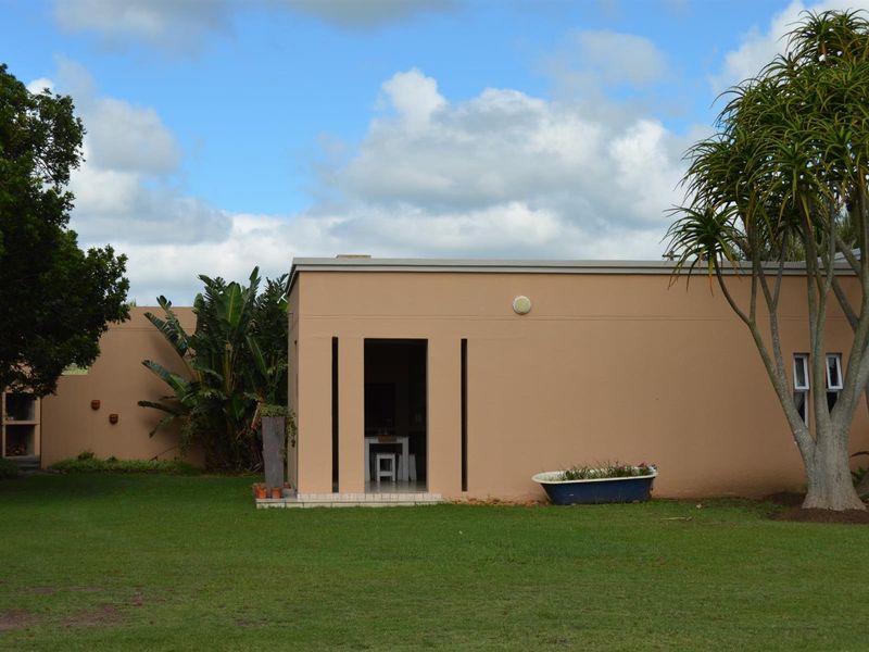 A view of the rear exterior of the property, featuring a well-maintained lawn, a tiled patio area, and a built-in outdoor braai facility.