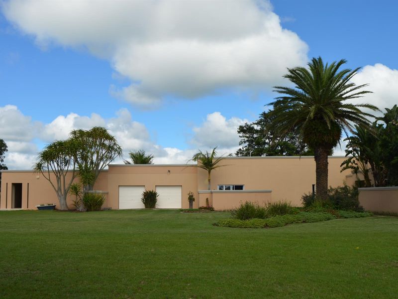 Front elevation of the property featuring a double garage, smooth rendered facade, and a well-maintained expansive lawn with established garden landscaping.