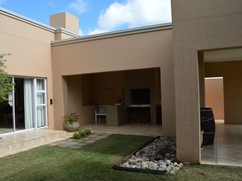 A covered patio area featuring a built-in braai, tiled flooring, and direct access to the garden through sliding glass doors.