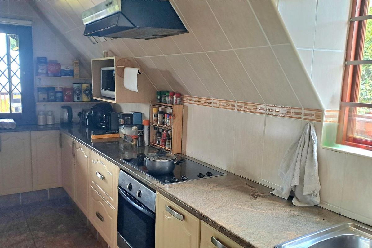A functional kitchen featuring granite countertops, built-in cabinetry, an electric hob, oven, and extractor fan, set under a sloped ceiling with natural light.