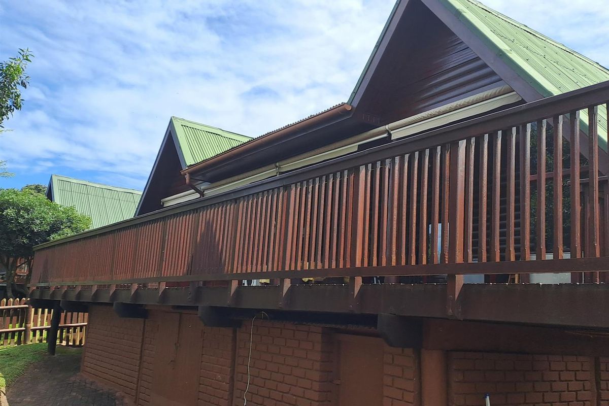 Rear view of the townhouse featuring a raised timber deck with balustrade, corrugated metal roofing, and a brick foundation wall.