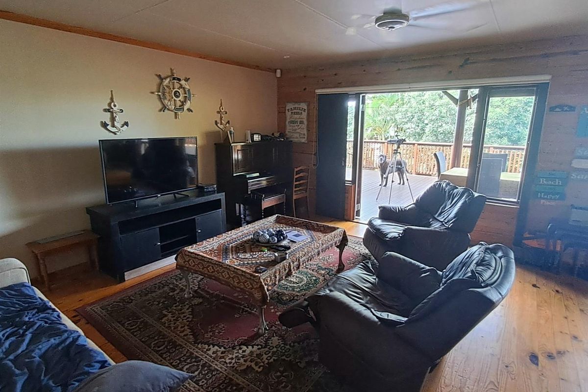 Spacious living room featuring timber flooring, wood-paneled walls, and large sliding glass doors that provide direct access to an outdoor deck area.