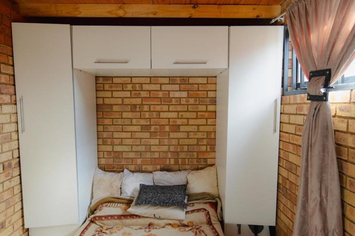A compact bedroom featuring exposed brick walls, built-in white cabinetry, and a wooden ceiling finish.