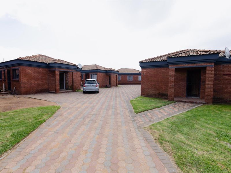 A view of a residential complex featuring multiple face-brick units with tiled roofs, paved driveways, and maintained lawn areas.