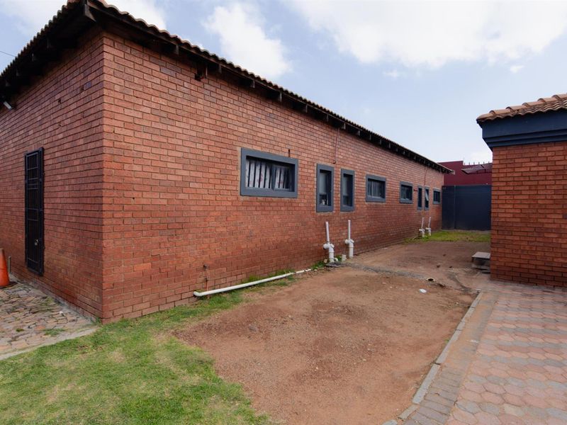 A view of the rear exterior of the house featuring red face-brick walls, tiled roofing, and paved pathways with an unlandscaped yard area.