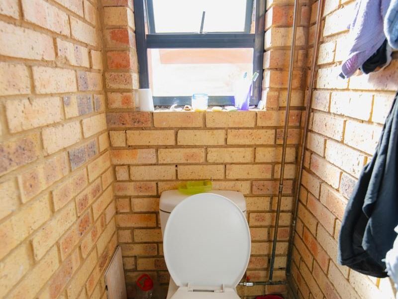 A compact bathroom featuring exposed brick walls, a standard toilet, and a small window providing natural light.
