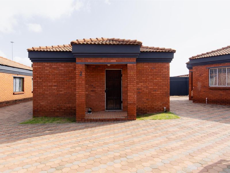 A well-maintained face-brick residential unit featuring a tiled roof, paved driveway, and secure entrance door.
