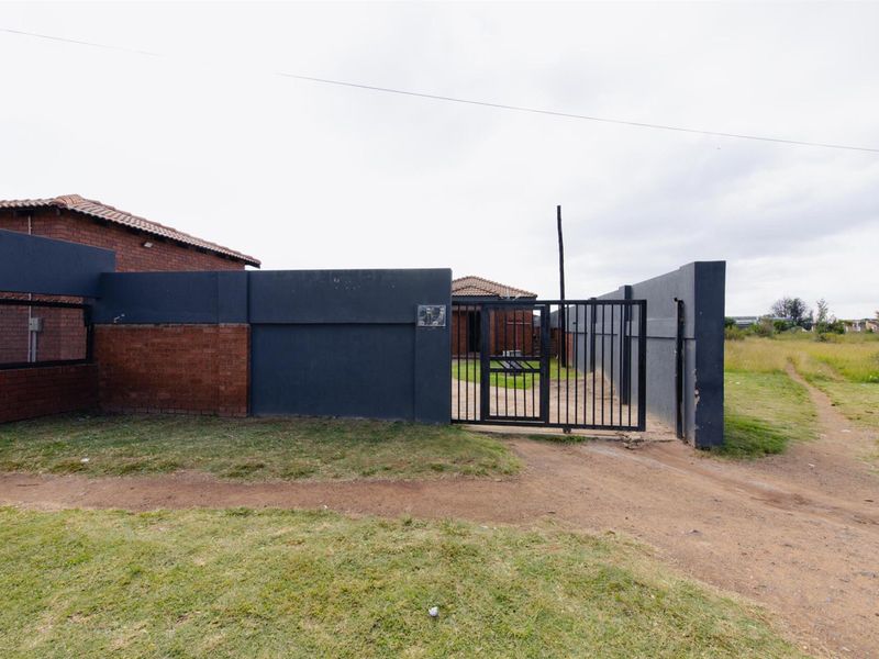 Front view of the property featuring a dark painted boundary wall, a metal security gate, and a tiled roof house structure.