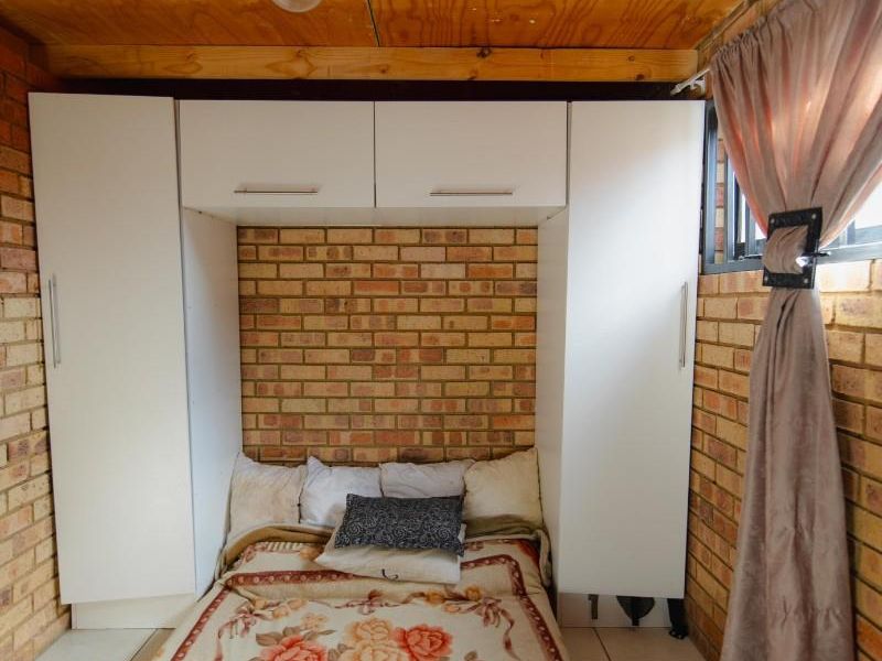 A compact bedroom featuring exposed brick walls, built-in white cabinetry, and a wooden ceiling finish.