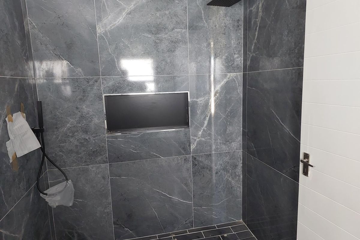 Modern walk-in shower featuring large format dark marble-look wall tiles, a built-in recessed niche, and contemporary black shower fixtures.