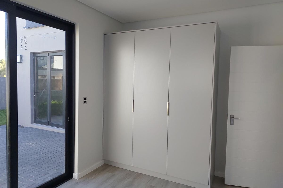 A bright, modern bedroom featuring a large built-in wardrobe, light laminate flooring, and a sliding glass door providing access to the outdoor patio area.