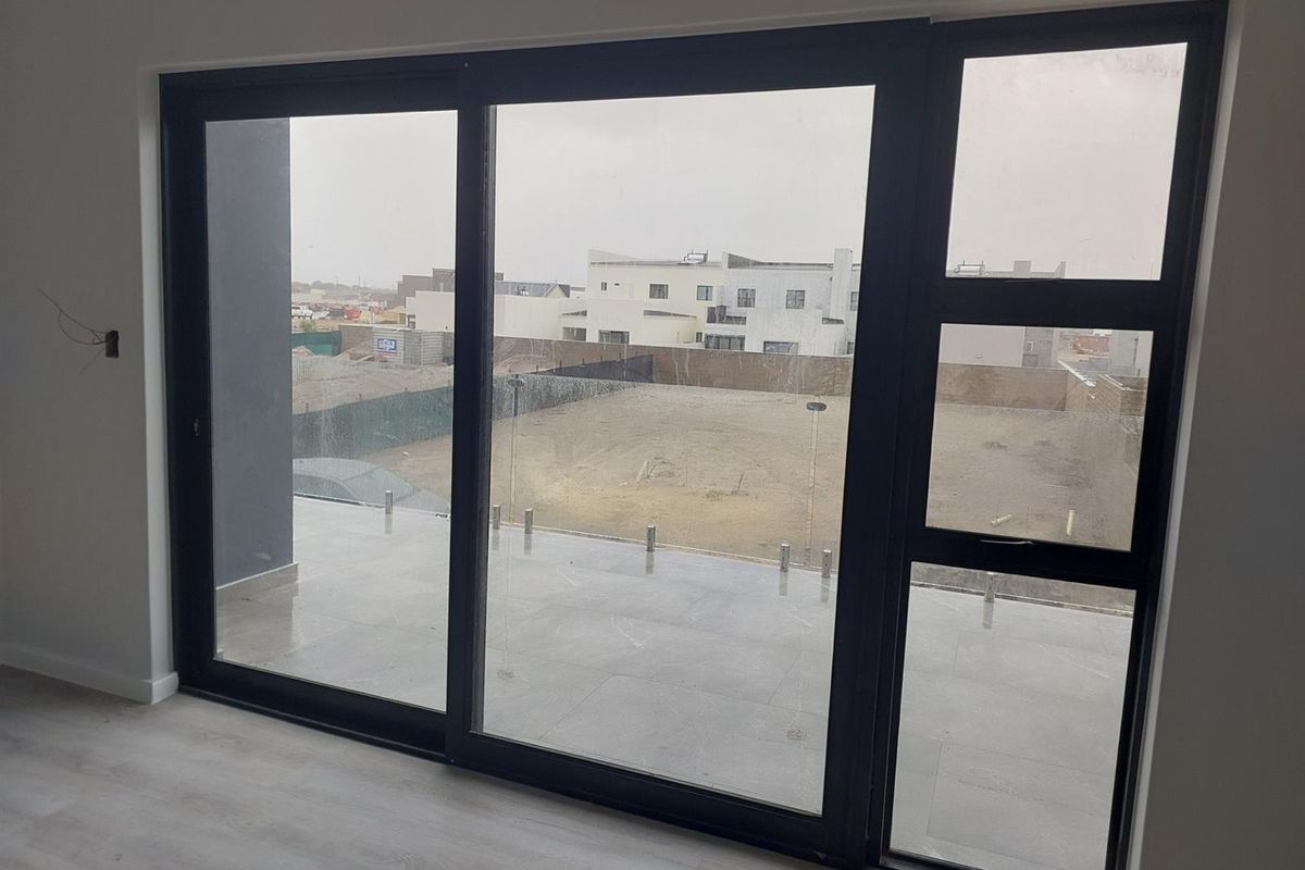 Bright living area featuring large sliding glass doors that open onto a tiled patio with a modern glass balustrade.