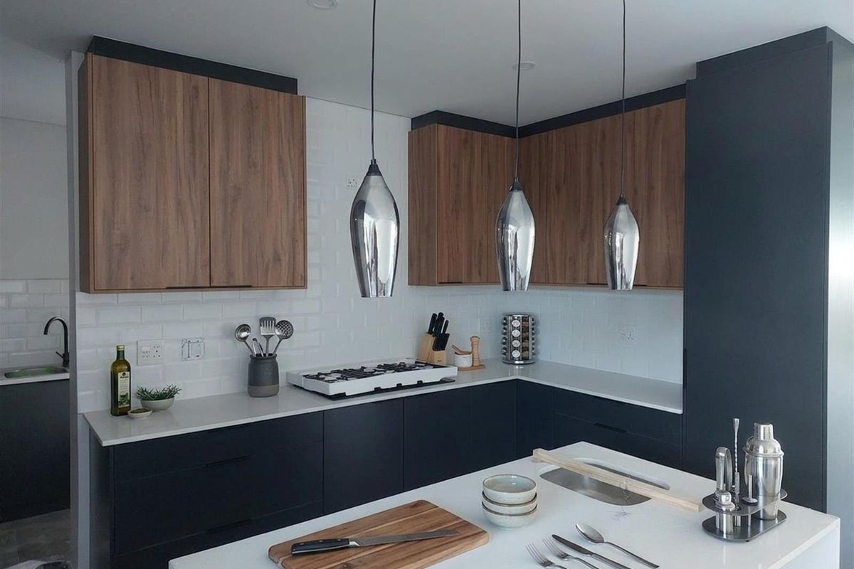 Modern kitchen featuring two-tone cabinetry, stone countertops, a central island with sink, gas hob, and stylish pendant lighting.