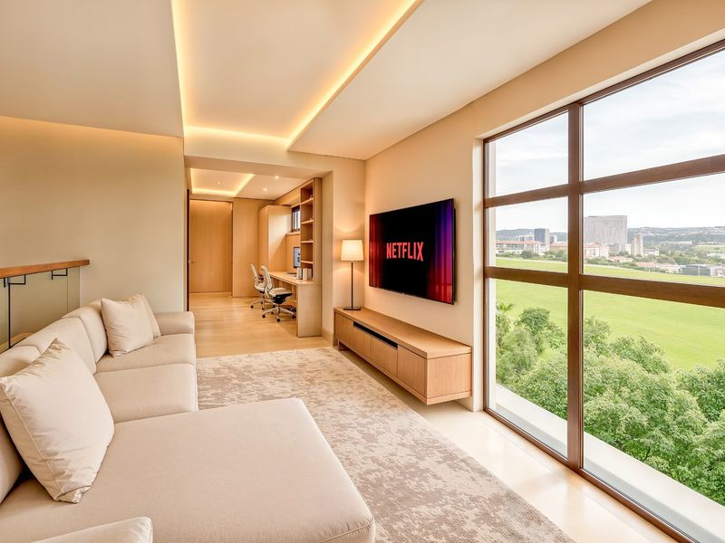 Modern living room featuring recessed ceiling lighting, built-in cabinetry, and large windows offering expansive views, seamlessly connected to a dedicated home office space.