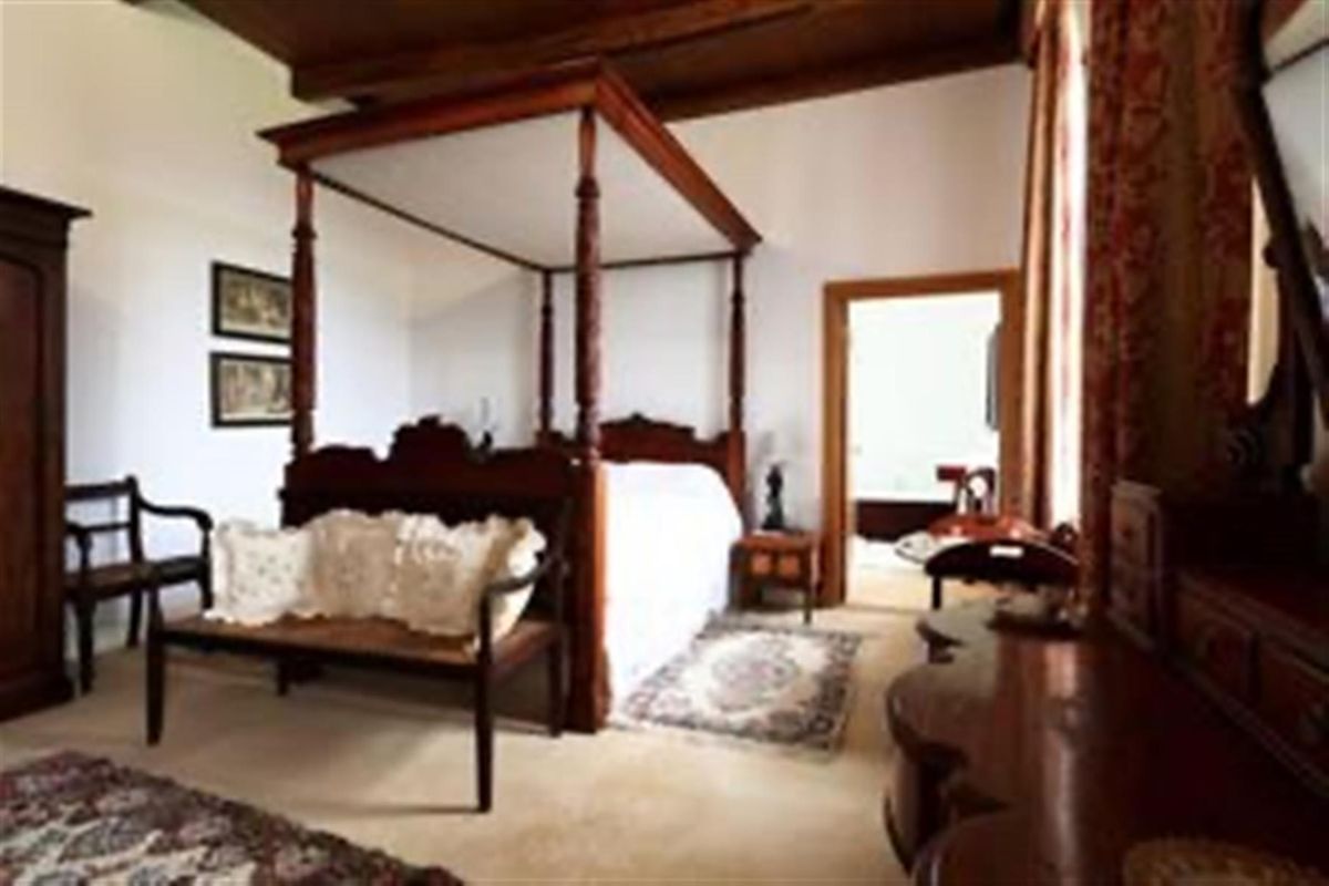 Spacious bedroom featuring high ceilings with exposed timber beams and an adjoining ensuite bathroom.