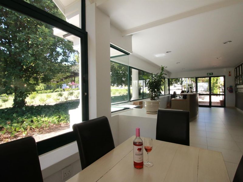 Bright open-plan living area featuring expansive floor-to-ceiling windows with garden views, tiled flooring, and a built-in service counter.