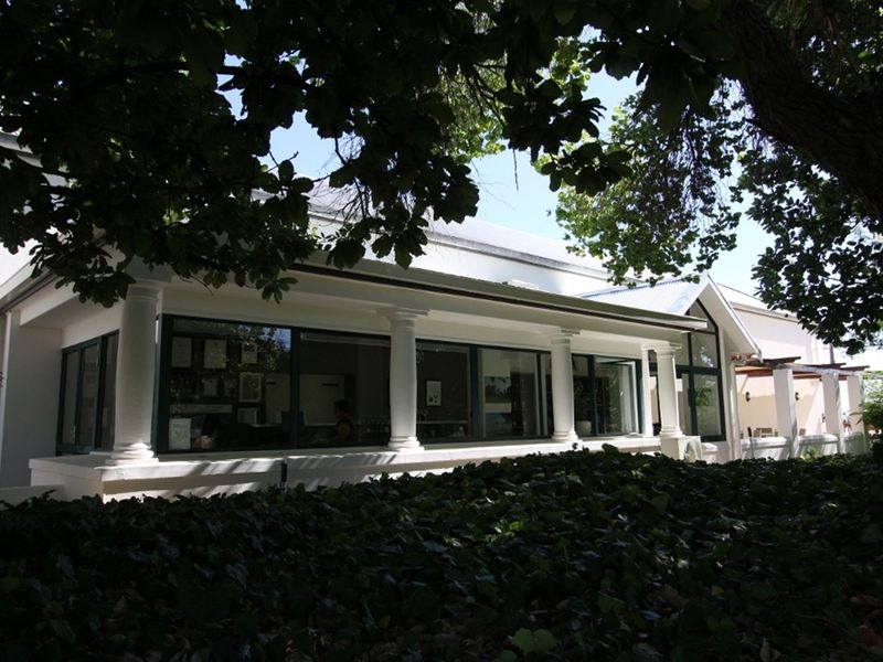 Rear view of the farm property featuring a covered patio with classical columns and large glass sliding doors, surrounded by mature trees.