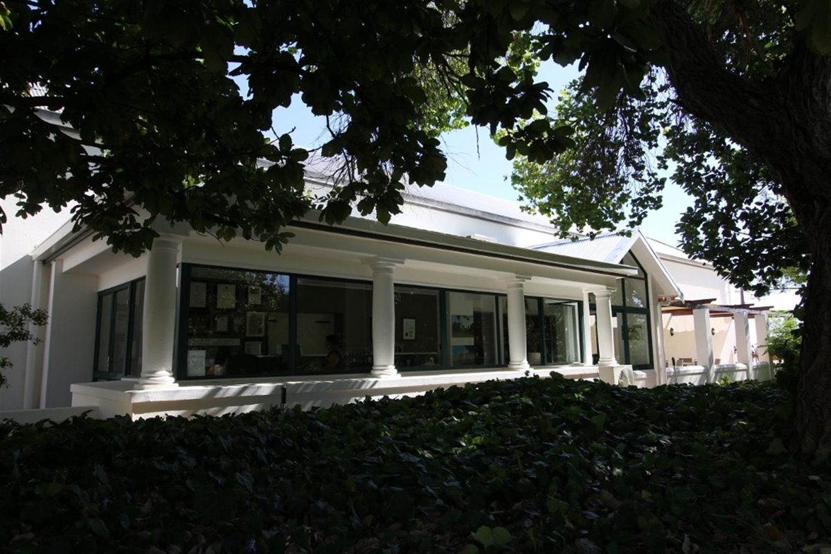 Rear view of the farm property featuring a covered patio with classical columns and large glass sliding doors, surrounded by mature trees.