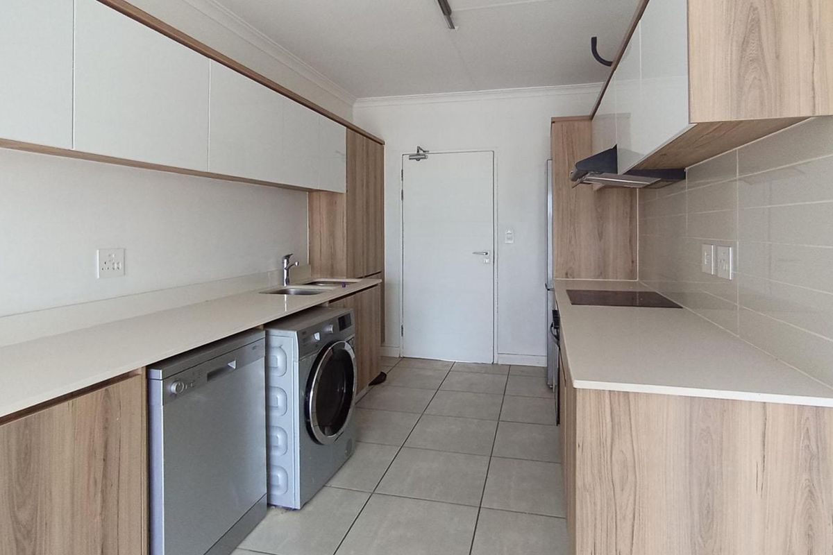 Modern galley-style kitchen featuring light wood-grain cabinetry, stone-look countertops, integrated hob, extractor fan, and dedicated space for laundry appliances.