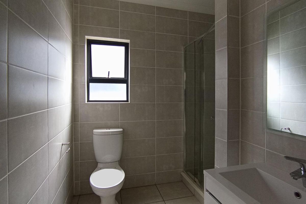 A modern bathroom featuring floor-to-ceiling neutral tiling, a glass-enclosed shower, a wall-mounted mirror, and a contemporary vanity unit.