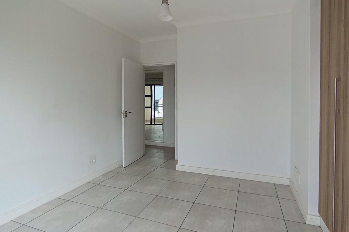 A bright, empty bedroom featuring neutral tiled flooring and built-in wooden cabinetry, offering a clean and versatile living space.