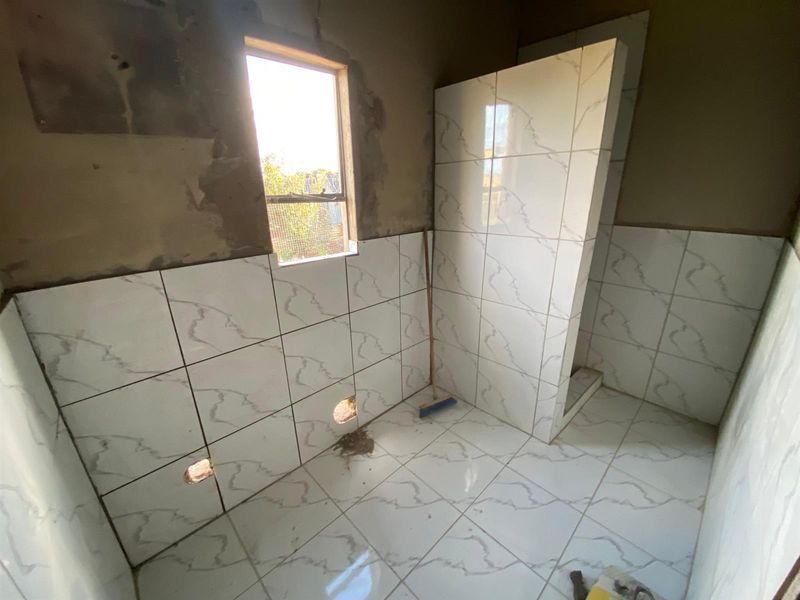 An unfinished bathroom space featuring partially tiled walls and floor, a shower partition wall, and an unplastered upper wall section.