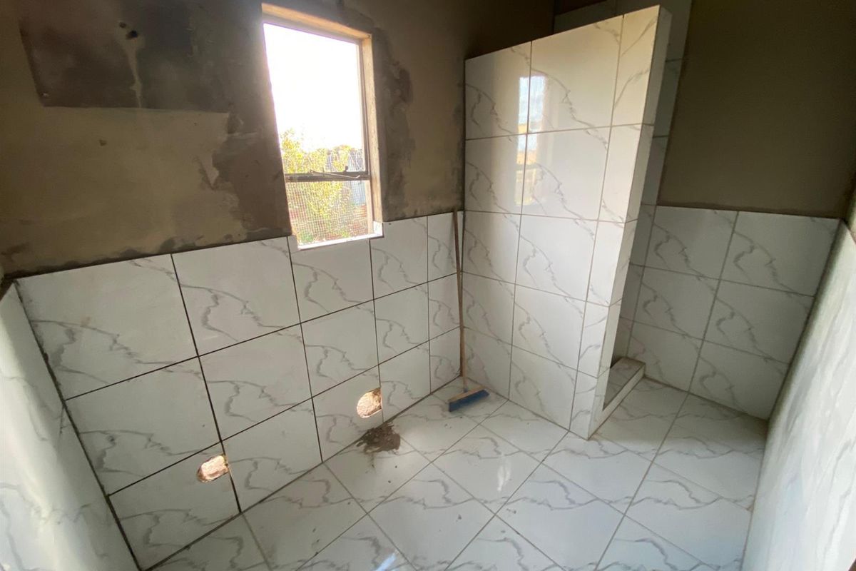 An unfinished bathroom space featuring partially tiled walls and floor, a shower partition wall, and an unplastered upper wall section.