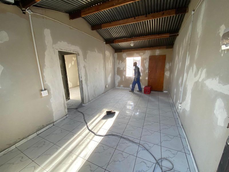 An unfinished living area featuring tiled floors, exposed corrugated metal ceiling with timber rafters, and surface-mounted electrical conduits, requiring final wall finishing.