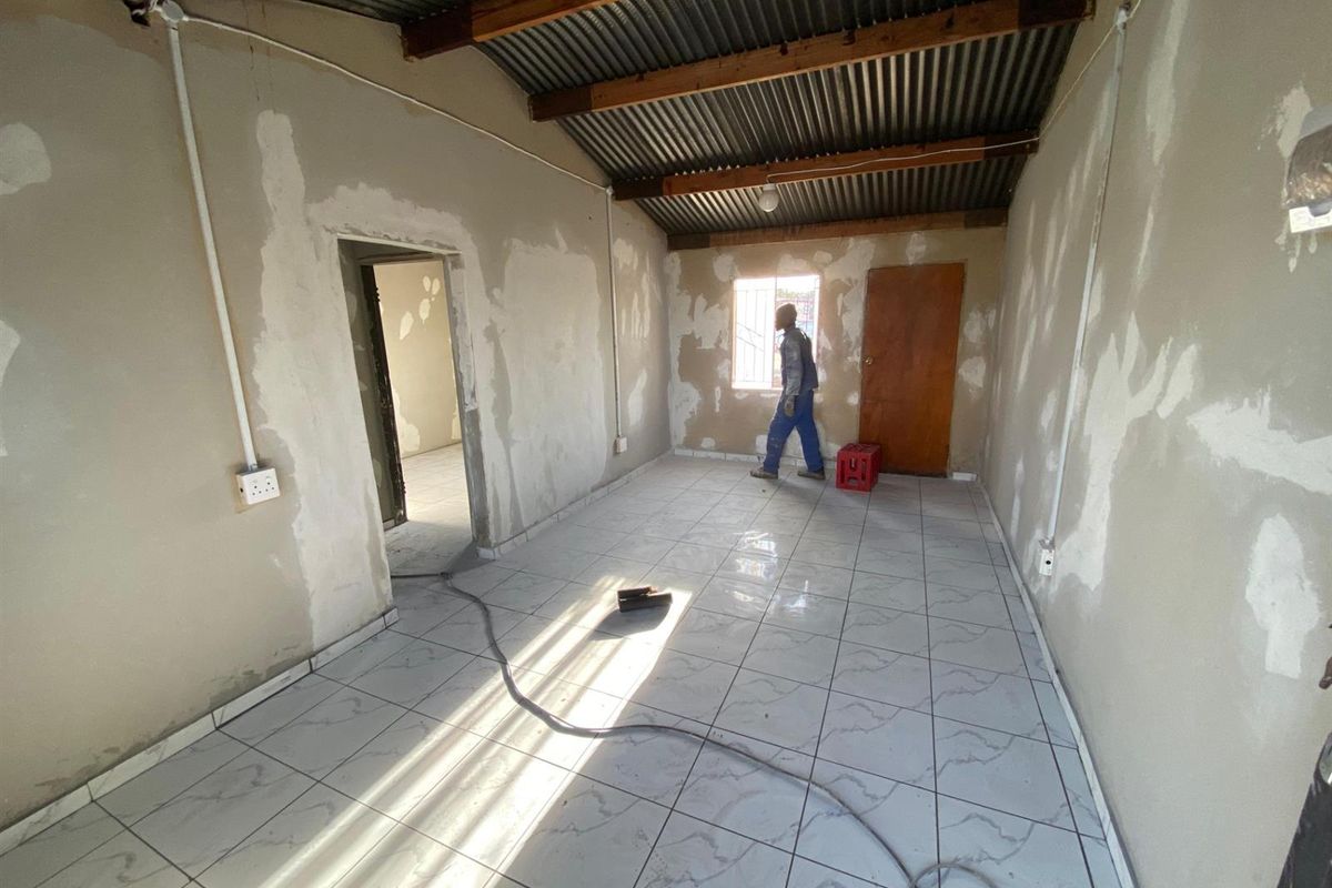 An unfinished living area featuring tiled floors, exposed corrugated metal ceiling with timber rafters, and surface-mounted electrical conduits, requiring final wall finishing.