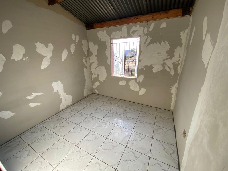 An unfinished bedroom featuring tiled flooring, security bars on the window, and an exposed corrugated metal ceiling, requiring final wall finishing and painting.