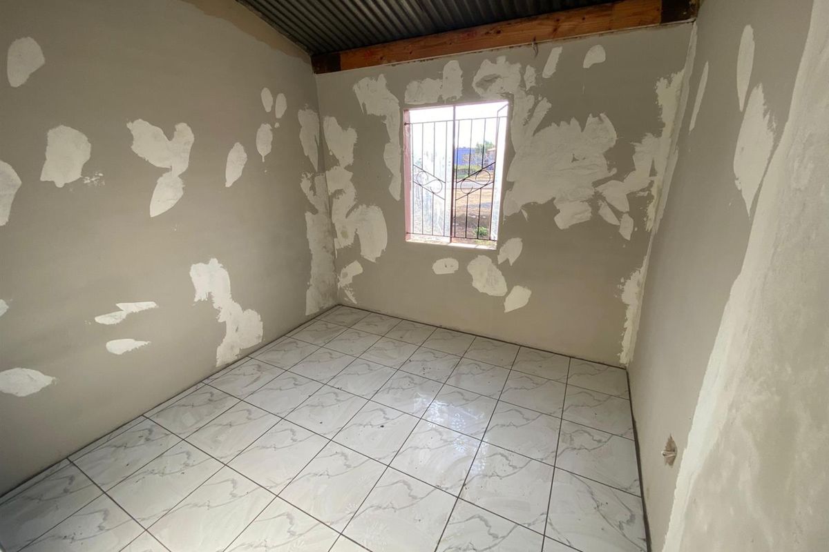 An unfinished bedroom featuring tiled flooring, security bars on the window, and an exposed corrugated metal ceiling, requiring final wall finishing and painting.