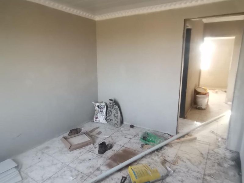 An empty bedroom currently undergoing renovation, featuring tiled flooring and ceiling cornice, requiring final finishing and cleaning.
