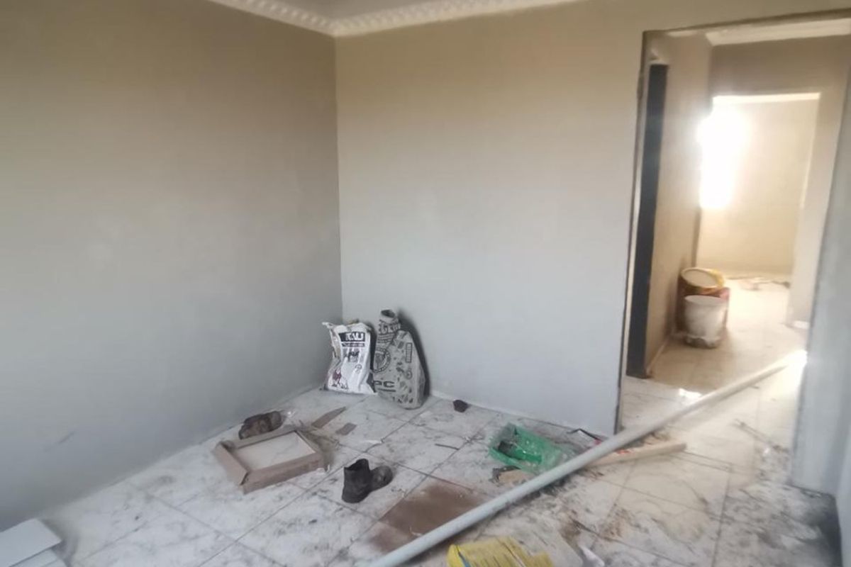 An empty bedroom currently undergoing renovation, featuring tiled flooring and ceiling cornice, requiring final finishing and cleaning.