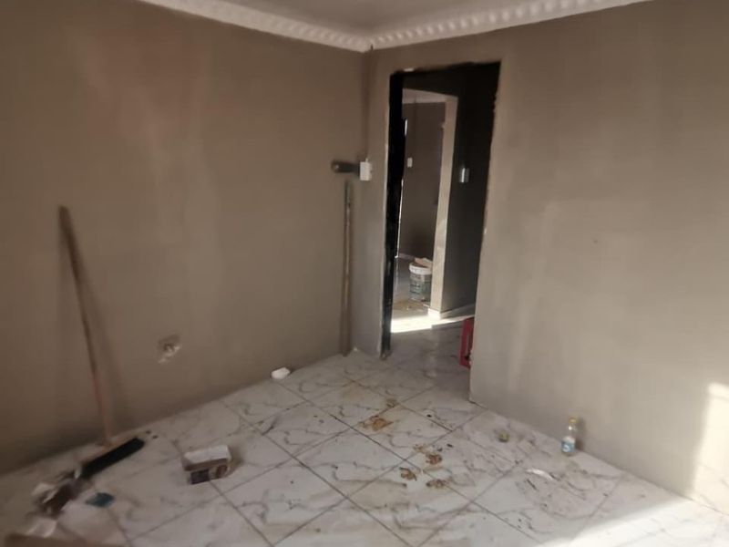 An unfinished living area featuring tiled flooring, decorative ceiling molding, and PVC ceiling panels, currently in need of final wall finishing and cleaning.