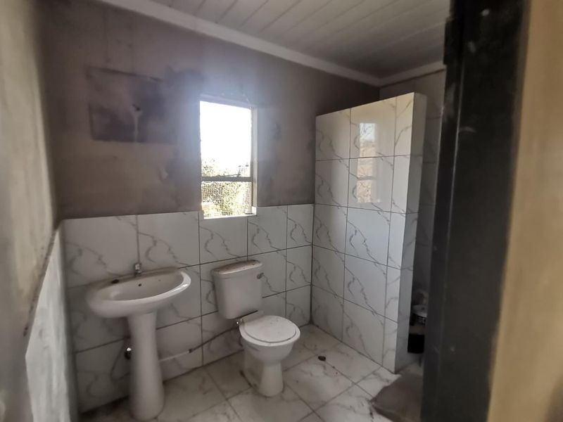 A bathroom in the process of renovation, featuring a pedestal basin, toilet, and tiled shower enclosure with unfinished wall surfaces.