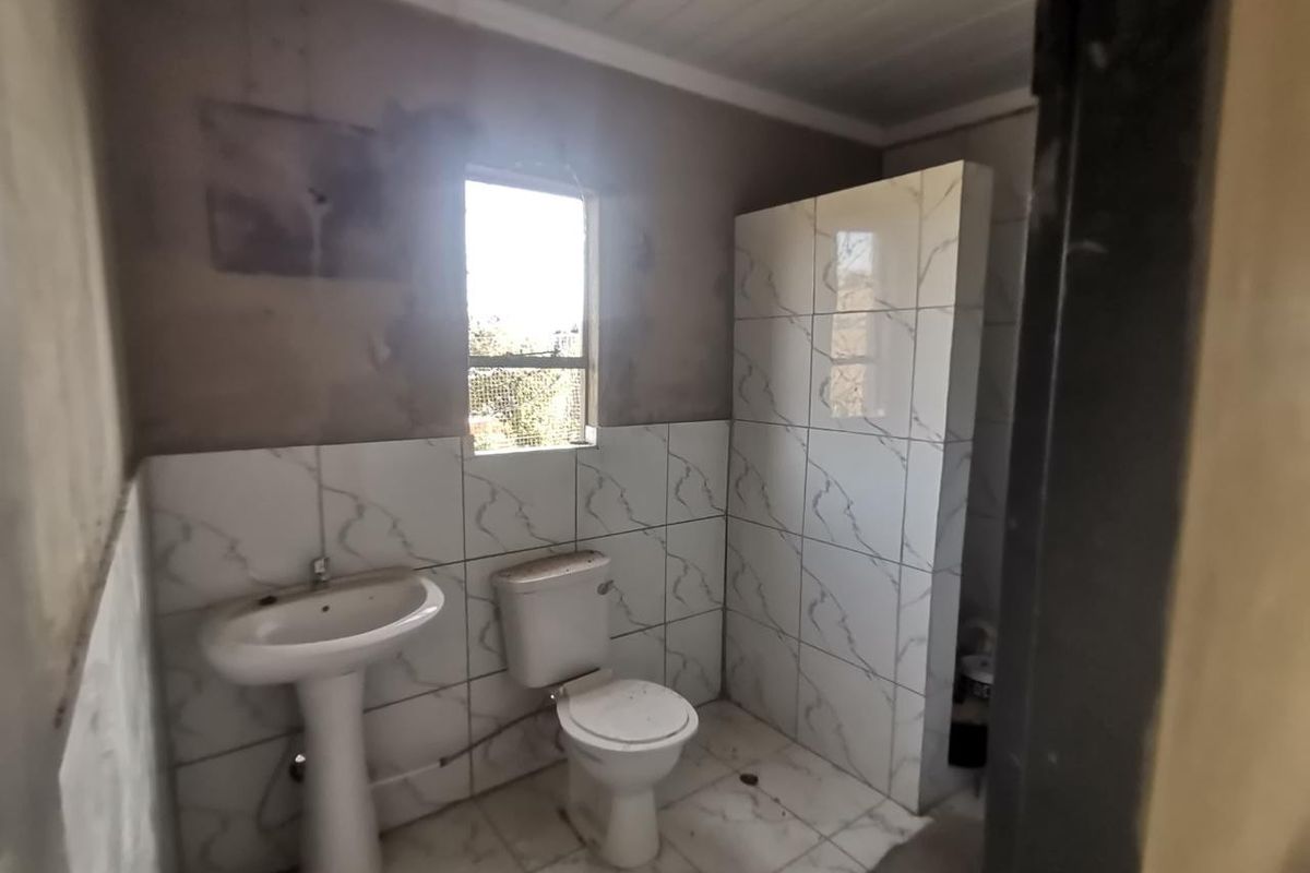 A bathroom in the process of renovation, featuring a pedestal basin, toilet, and tiled shower enclosure with unfinished wall surfaces.
