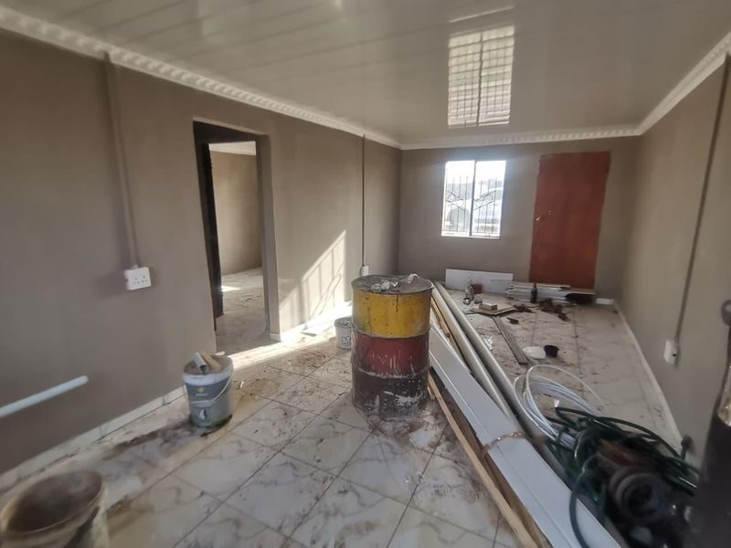 An unfinished living area featuring tiled floors, PVC ceiling panels with cornice, and security bars on the window, currently undergoing renovation.