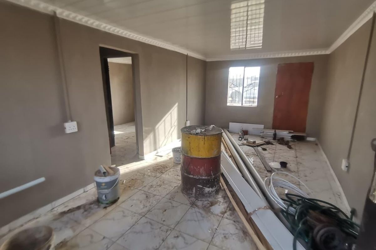 An unfinished living area featuring tiled floors, PVC ceiling panels with cornice, and security bars on the window, currently undergoing renovation.