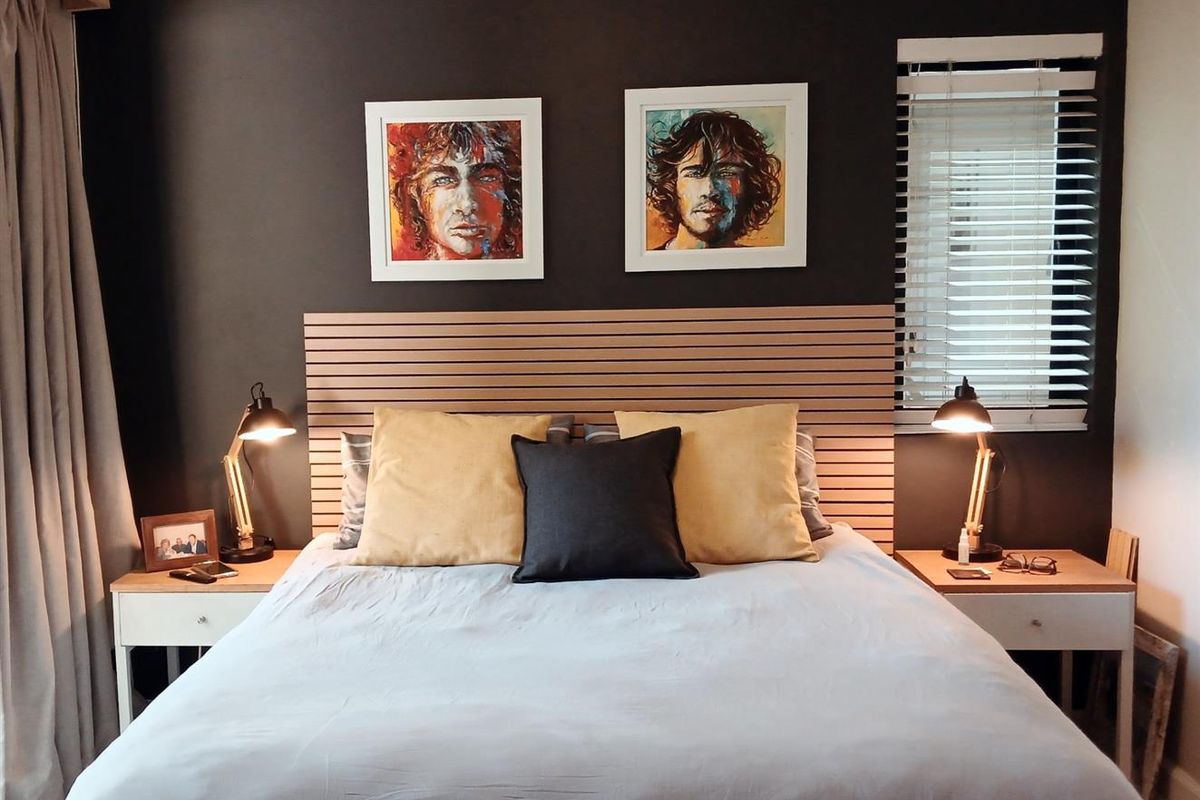 A well-appointed bedroom featuring a horizontal slat headboard, dark accent wall, and integrated window blinds.