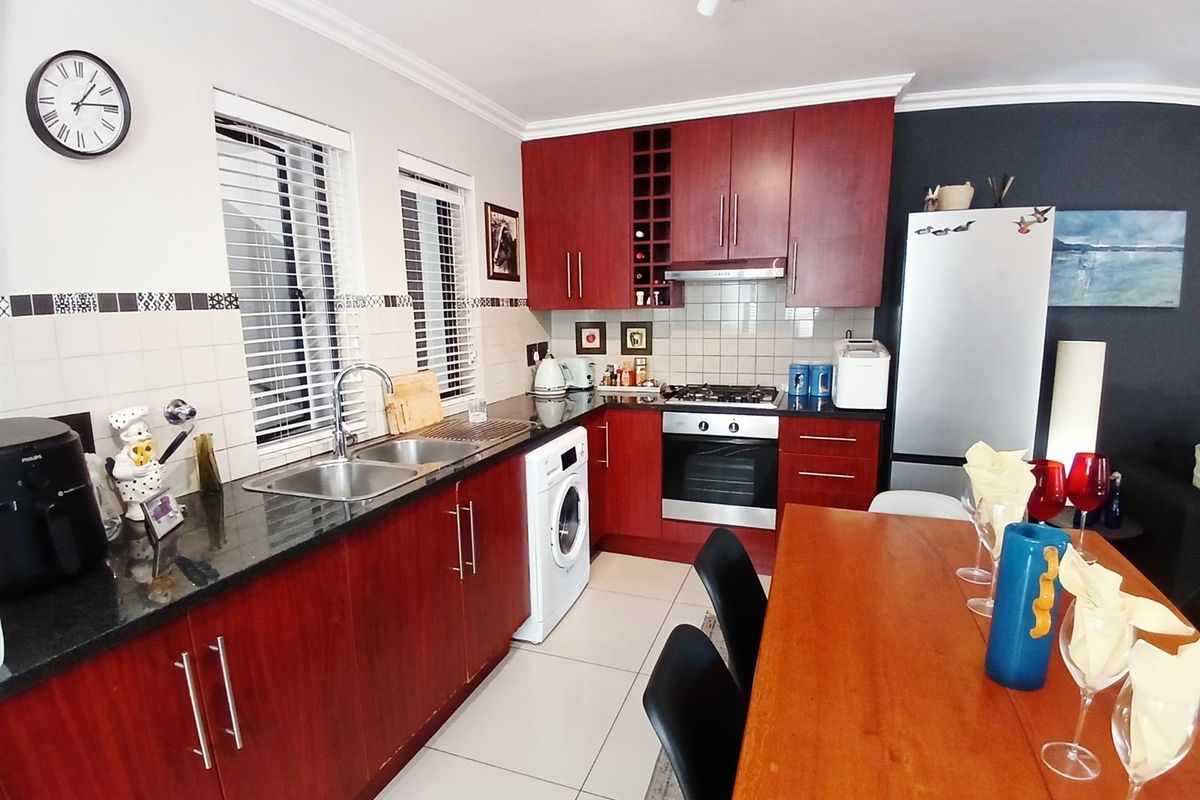 A functional kitchen featuring dark wood cabinetry, granite countertops, a built-in oven, gas hob, extractor fan, and integrated laundry appliance space.