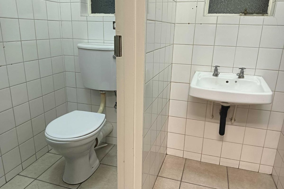 A functional commercial restroom featuring a wall-mounted basin and a standard toilet, finished with white wall tiles and neutral floor tiling.