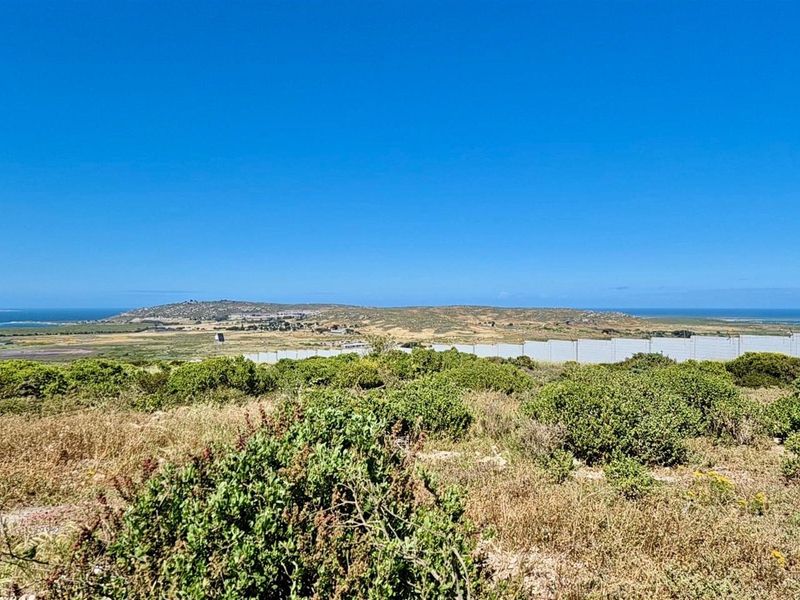 A wide-angle view of the vacant residential land, showcasing the surrounding landscape, natural vegetation, and distant coastal horizon.