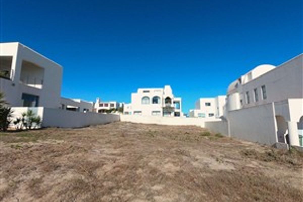 A vacant plot of land situated between existing residential properties, featuring boundary walls and clear access to surrounding structures.