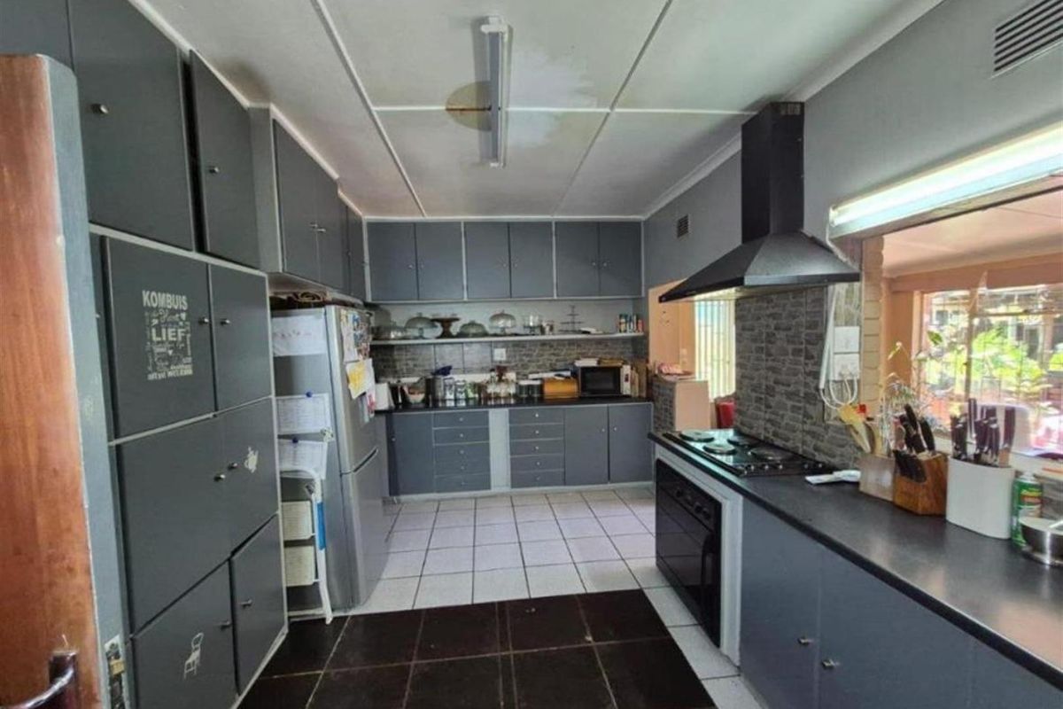 A functional kitchen featuring grey cabinetry, a built-in oven, a gas hob with an extractor fan, and tiled flooring.