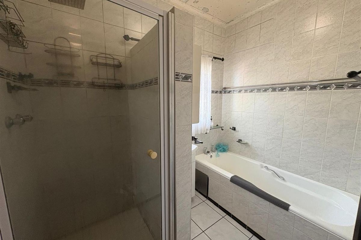 A functional bathroom featuring a separate shower enclosure, a built-in bathtub, and tiled walls, currently showing signs of ceiling wear.