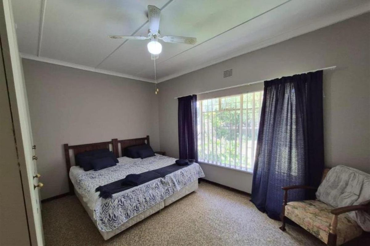 A functional bedroom featuring a large window with security bars, neutral wall tones, and a ceiling fan.