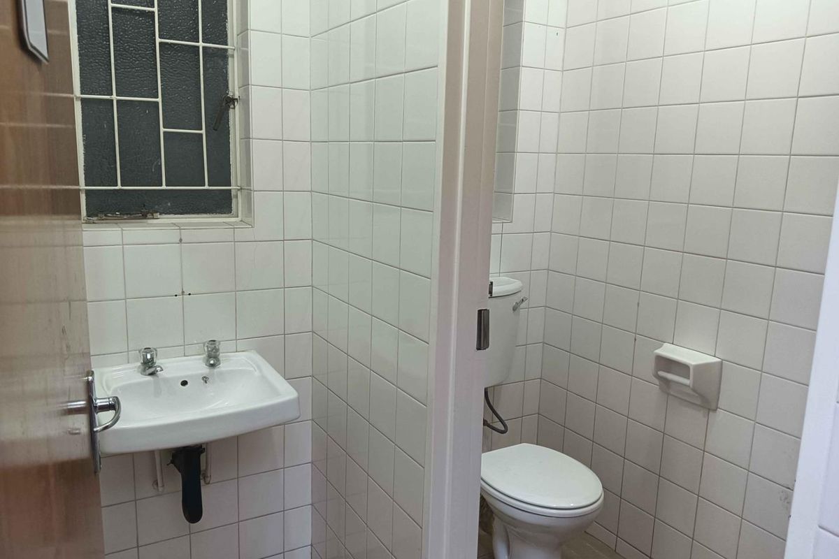 A functional commercial restroom featuring white wall tiles, a wall-mounted basin, and a standard toilet suite with a privacy partition.